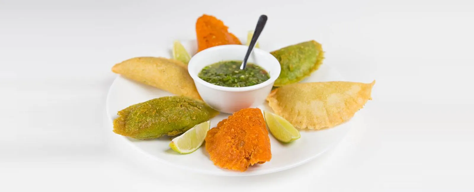 A platter of golden Colombian empanadas with lime and ají